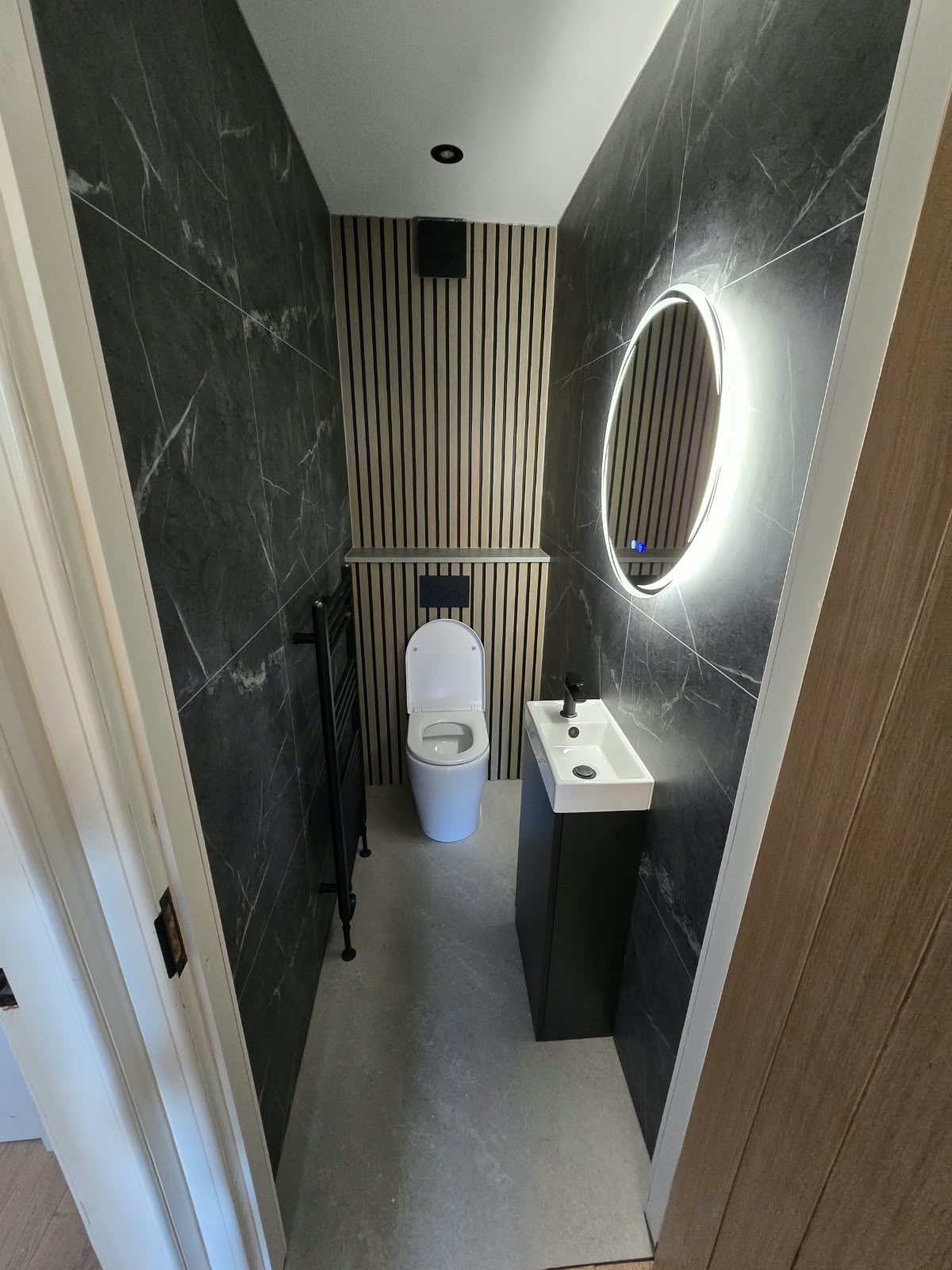 Narrow bathroom with a lit round mirror